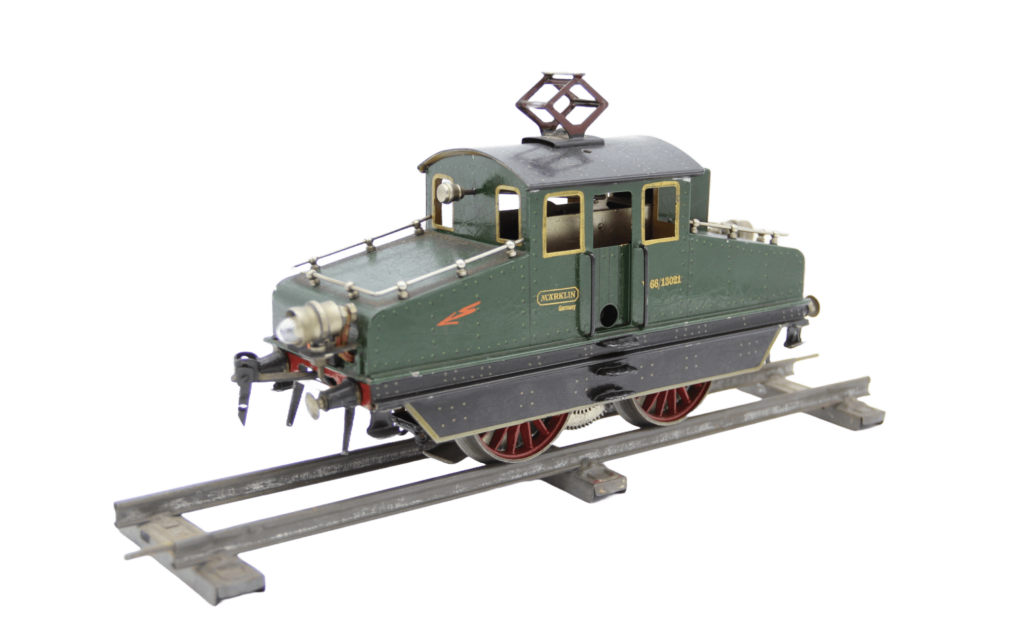Modell einer Elektrolokomotive mit der Nummer 66/13021, Stromabnehmer (Pantograph), roten Speicherrädern und Märklin-Logo an der Seite. Die Farbgebung ist dunkelgrün mit schwarzen und goldfarbenen Zierdetails.
