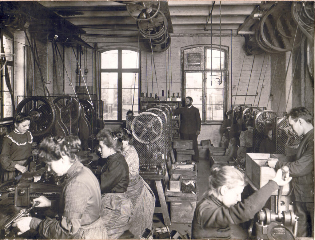 Ein Vorarbeiter leitet Arbeiter und Arbeiterinnen beim Blechstanzen an.