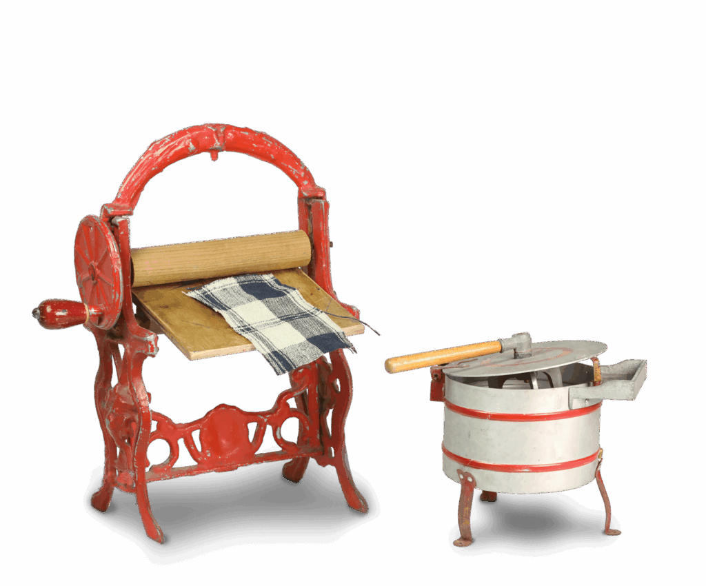 Miniatur-Gerät aus rotem Blech, in dessen Mittelpunkt eine Rolle aus Holz steht, die mit einer Kurbel betätigt werden kann. Auf einer hölzernen Ablage unterhalb der Rolle liegt ein Stück Stoff. Daneben ein silberner Kessel auf drei Füßen und einem Deckel, der mit einem länglichen Griff angehoben werden kann.