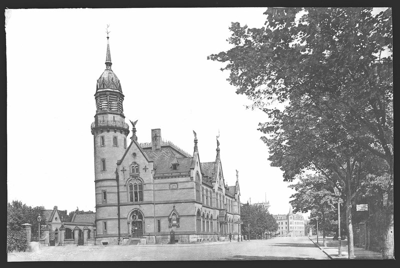 Architektonisch reich verziertes Geböude mit einem Turm und mehreren Giebeln auf der Längsseite.
