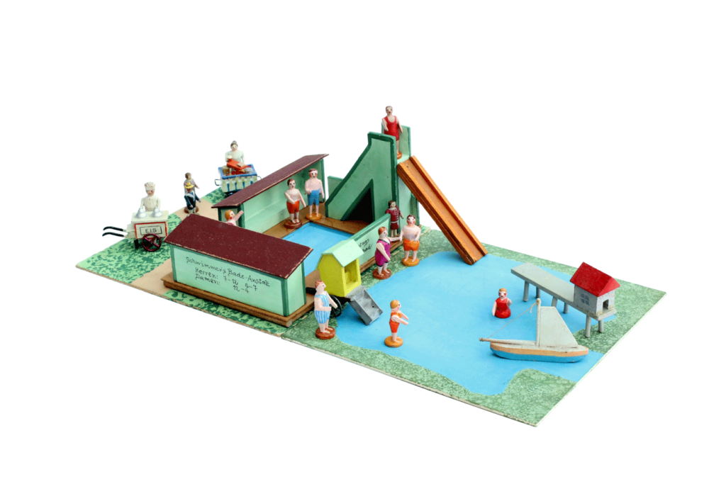 Miniatur-Modell eines Schwimmbads mit Wasserrutsche, Badesteg, Boot, Badegästen sowie Eis- und Getränkewagen.
